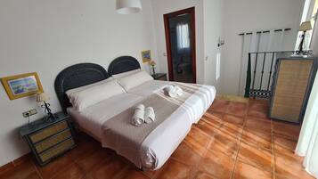 A neatly made bed with pillows and towels, a bedside table with a lamp, a framed picture on the wall, and a bathroom visible through an open door.