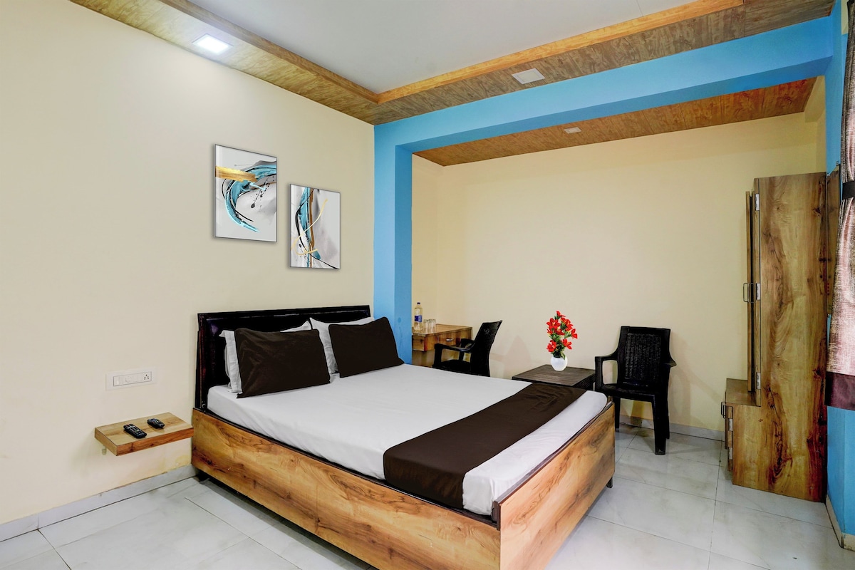 A bedroom with a wooden bed, a desk, and two chairs. There are two paintings on the wall.