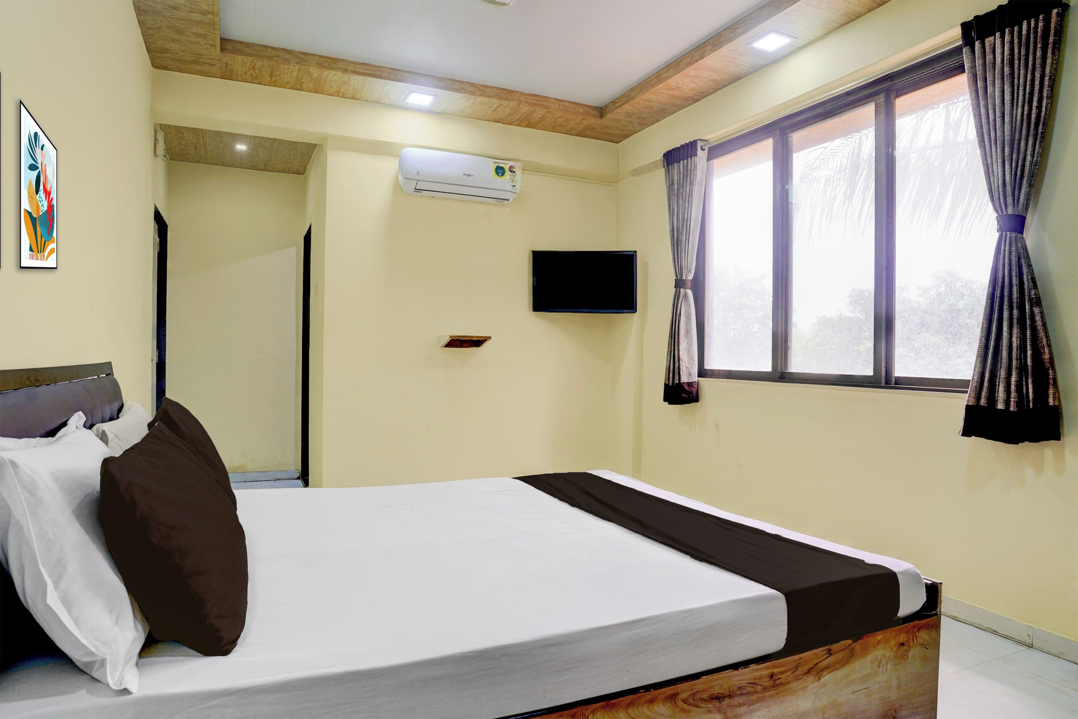 Una habitación de hotel con una cama, televisión, ventana con cortinas y equipo de aire acondicionado.