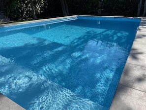 Ein rechteckiger Swimmingpool mit klarem, blauem Wasser, umgeben von einer gefliesten Liegefläche.