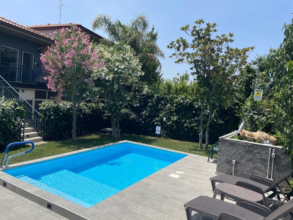 Une piscine dotée d’une terrasse carrelée, entourée d’arbres et bordée d’un bâtiment avec un balcon.