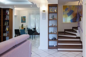 A living room with a sofa, a dining area with chairs and a table, a staircase, and a bookshelf with various items. - CasaNova • Jacuzzi • 9 guests • 4 bedrooms (Zona Industriale)