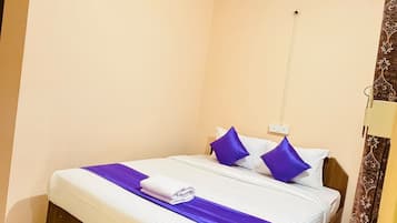 Una cama individual con estructura de madera, ropa de cama blanca y detalles morados.