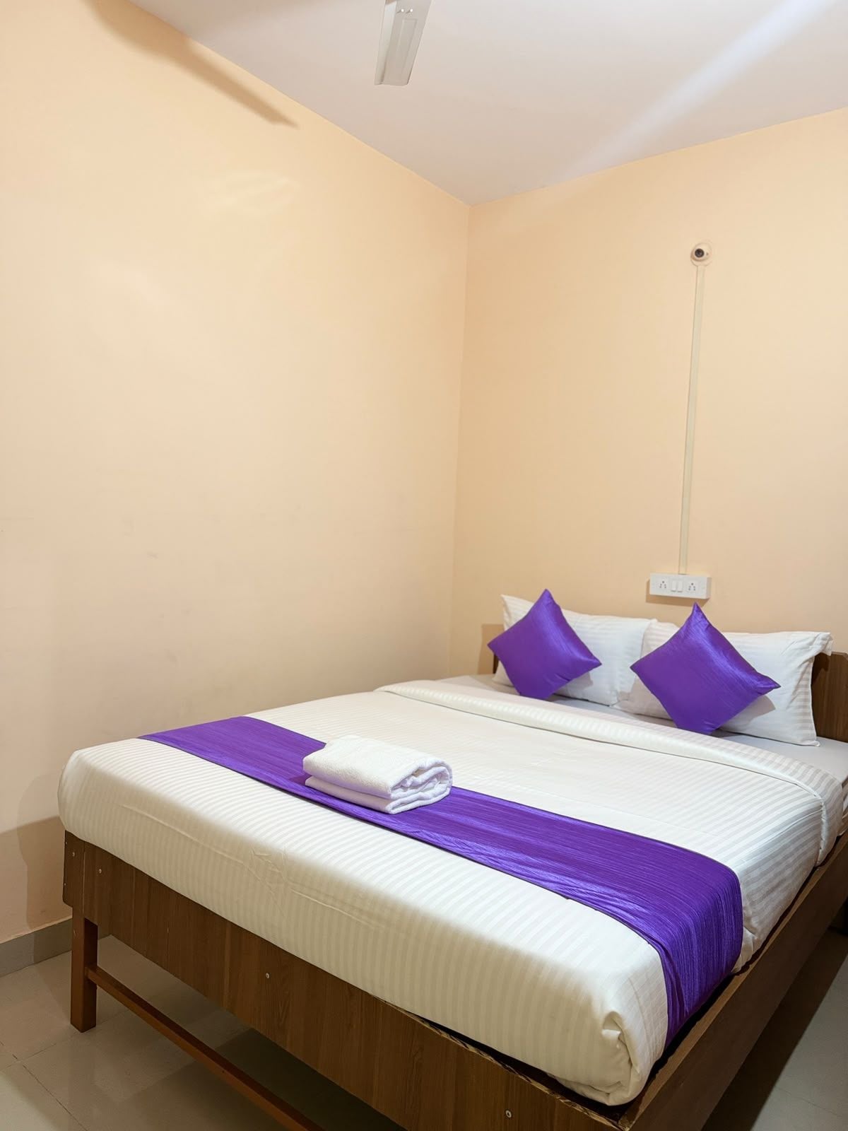 Una cama individual con estructura de madera, ropa blanca y detalles morados.