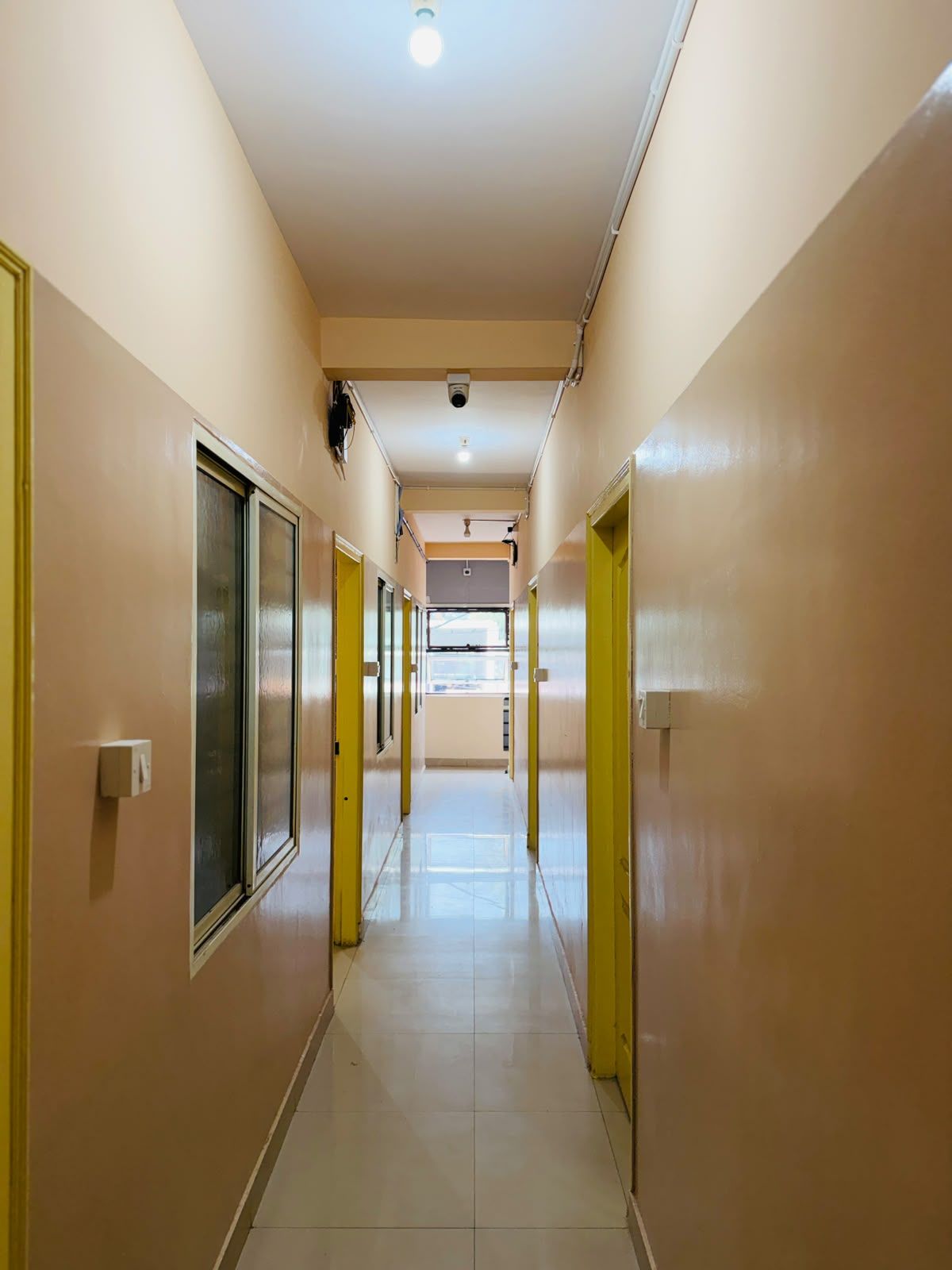 Un pasillo con puertas a ambos lados, una luz en el techo y una cámara de seguridad.