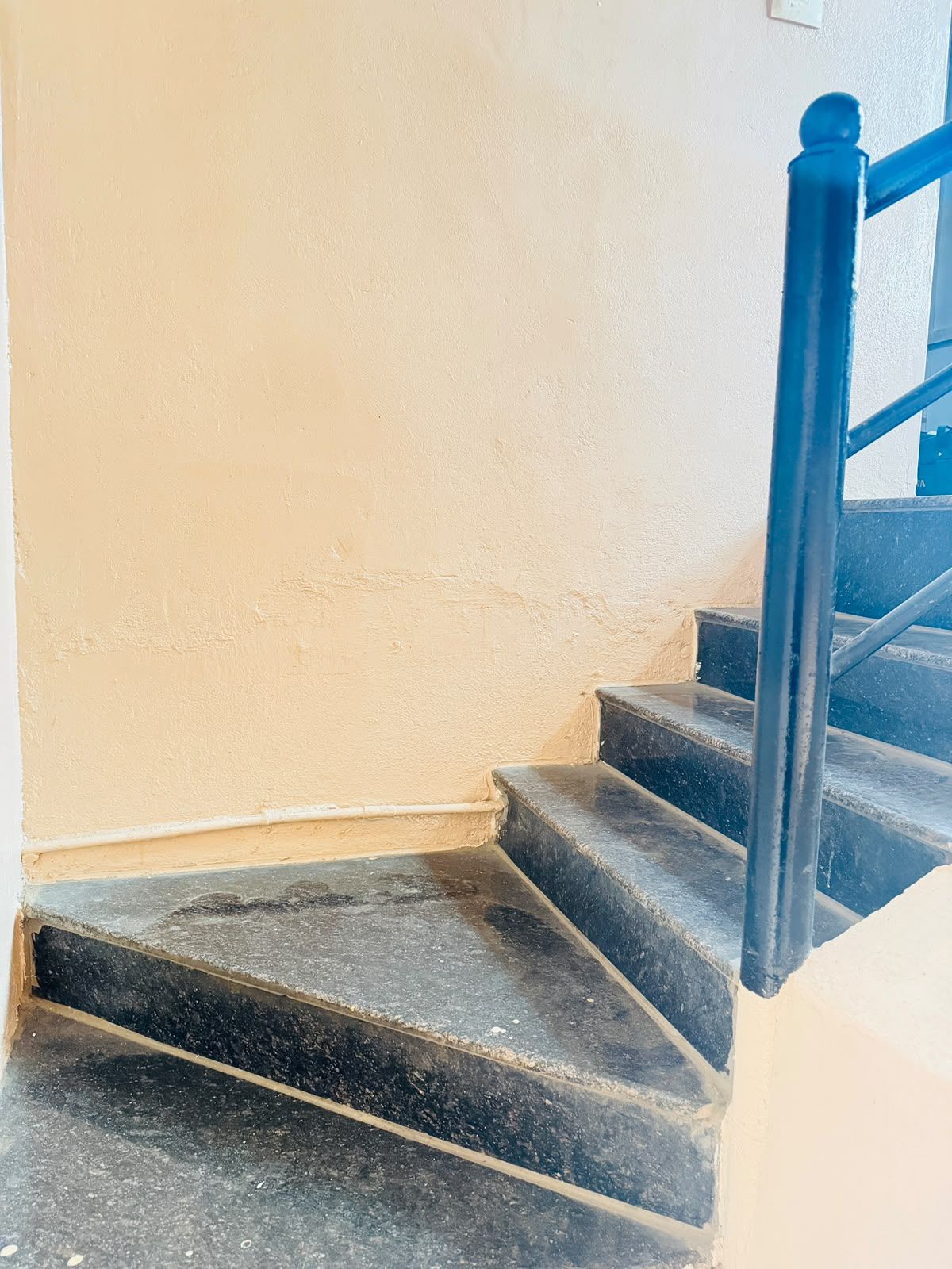 Una escalera con peldaños negros y barandilla azul que lleva a una plataforma.