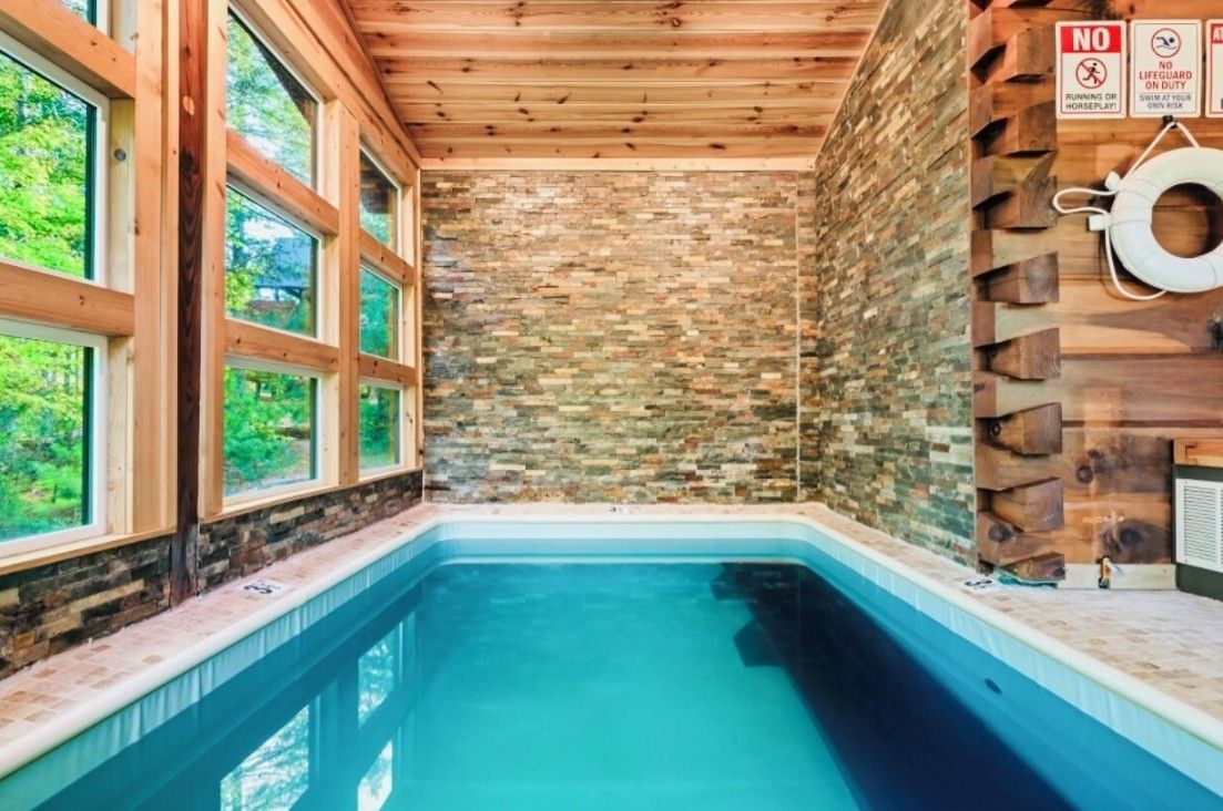 A swimming pool with a stone wall and wooden ceiling, surrounded by windows.