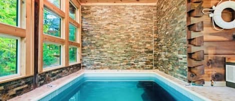 A swimming pool with a stone wall and wooden ceiling, surrounded by windows.