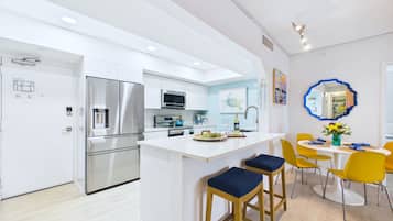 Una cocina moderna con electrodomésticos de acero inoxidable, una isla central con taburetes y un comedor con sillas amarillas.