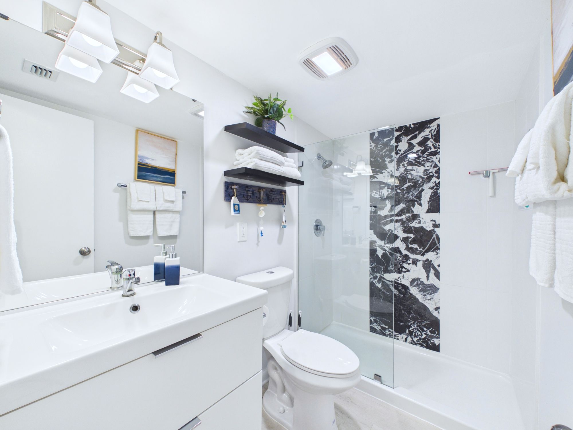 A modern bathroom with a white vanity, a glass shower enclosure, and a marble backsplash.