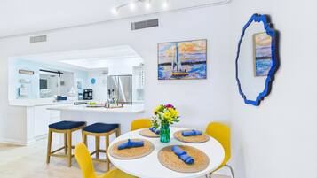A modern kitchen with white cabinets, a central island, and a dining area with yellow chairs and a white table.