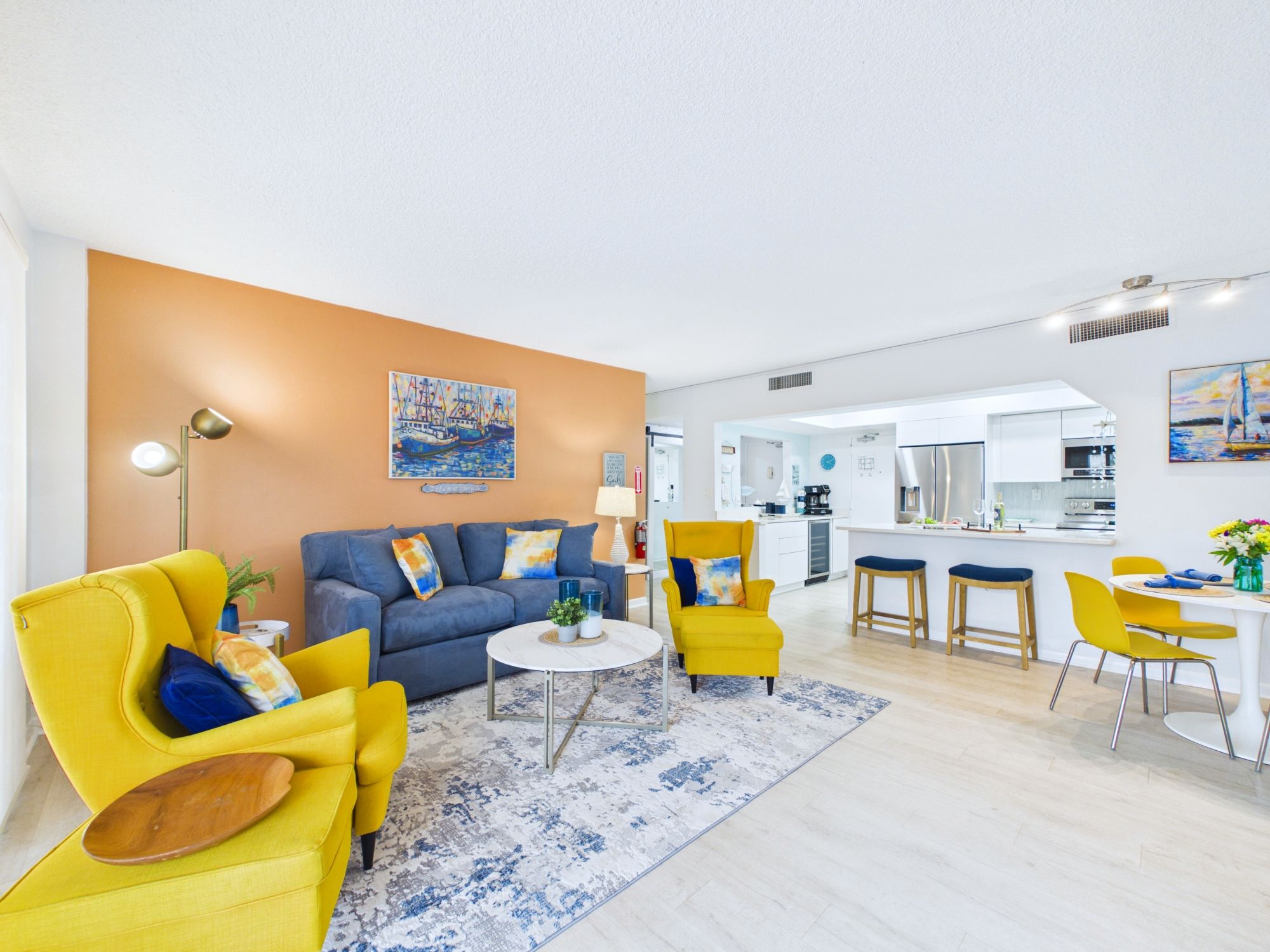 A modern living room with a sofa, armchairs, a coffee table, and a kitchen in the background.