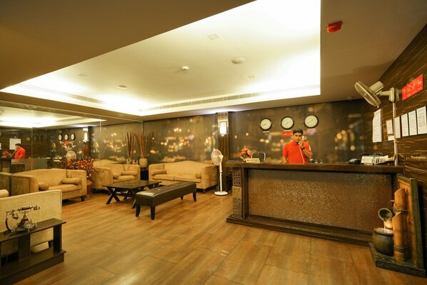A hotel lobby with sofas, a reception desk, and a clock on the wall.