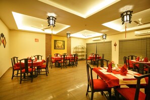 A dining area with multiple tables and chairs, ceiling fans, and traditional wall decorations.
