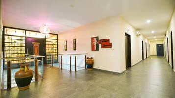 A hotel lobby with a reception desk, a glass partition with plants, a traditional vase, and a wall-mounted sign.