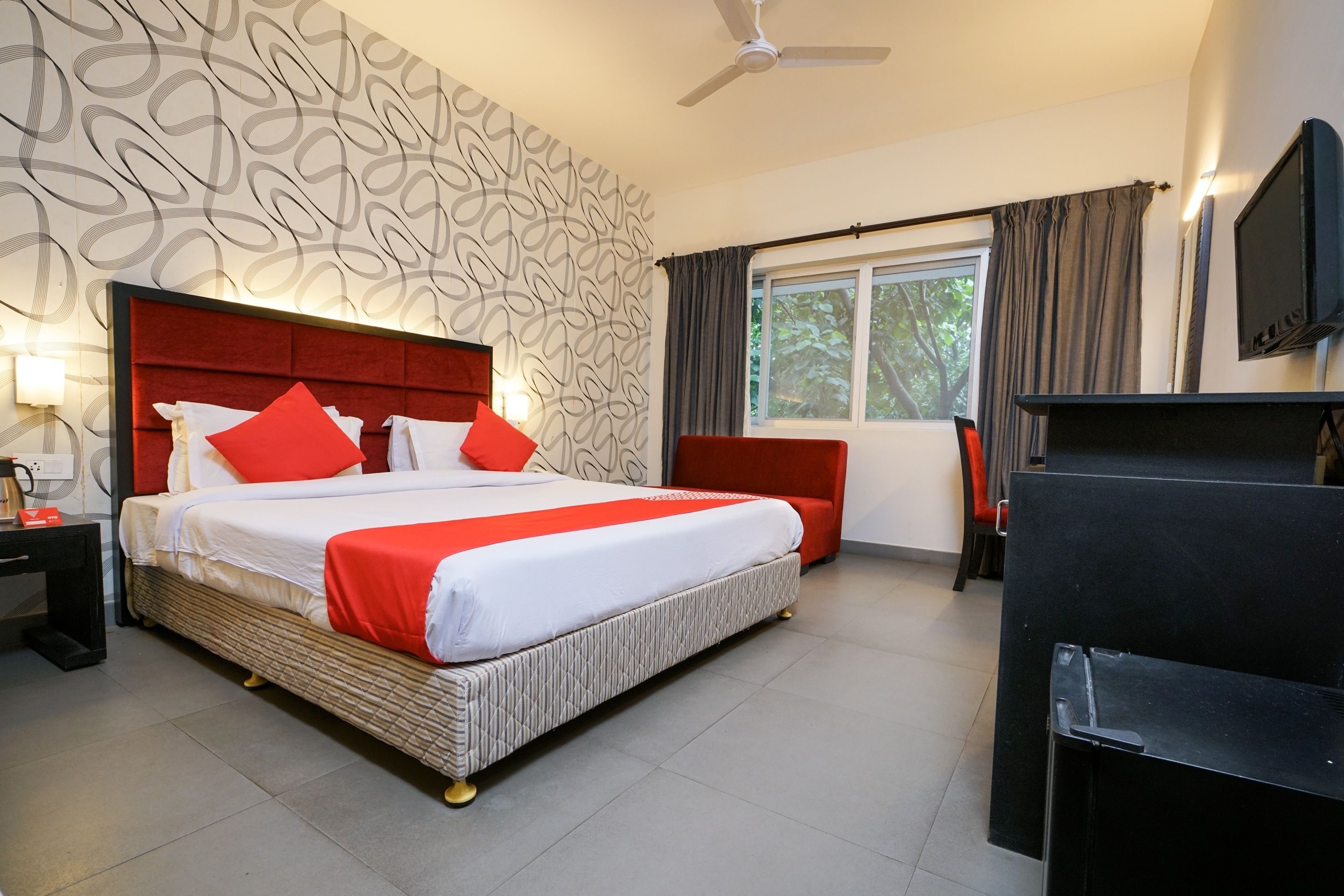 A hotel room with a large bed, a television, a desk, and a window with curtains.