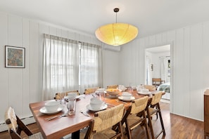 Een eetkamer met een houten tafel voor zes personen, witte stoelen en een hanglamp.