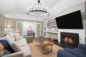A living room with a fireplace, a television, a chandelier, and a bookshelf. - Pondside Home | Hot Tub • Fire Pit • Beach Access (Greenwood Lake)