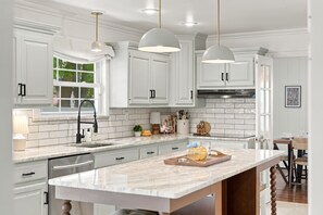 A modern kitchen with white cabinetry, a marble island, pendant lighting, and a view of the outdoors. - Pondside Home | Hot Tub • Fire Pit • Beach Access (Greenwood Lake)