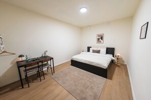 A bedroom with a bed, bedside table, lamp, and a desk with chairs. - Ghent for Four 2 Private King Bed Rooms (Ghent)