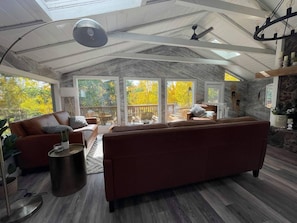 A spacious living area with a large sofa, a coffee table, and a view of the outdoors through large windows. - Sundance Festival Cabin – 30 Min to Boulder! Peaceful meadow• 4 BR• Ski Eldora  (Golden)