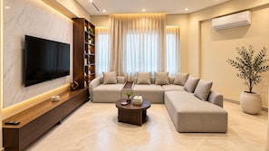A modern living room with a flat-screen TV, a sectional sofa, a coffee table, and a bookshelf. - NOMA Mohandessin (Giza Governorate)