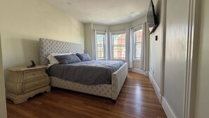 A bedroom with a bed, nightstand, and a flat-screen TV mounted on the wall. - 3-bedroom house in South Boston on a quiet side street, steps from everything (Boston)