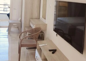 A room with a flat-screen TV mounted on the wall, a wicker chair, a wooden bench, and a remote control on the bench. - Pool View Studio Tiba Golden Resort (Hurghada)