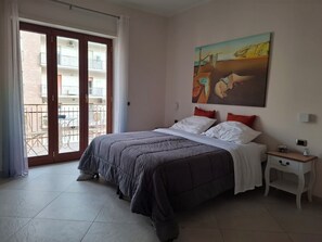 Ein Schlafzimmer mit einem Bett, einem Nachttisch, einem Gemälde und Blick auf den Außenbalkon.
