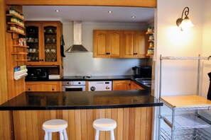 A kitchen with wooden cabinets, a black countertop, two white stools, and a stainless steel range hood. - Makers Rest a relaxing 4BR 3Bath for 6 with its own Poolfresh Wellness Retreat (Wynyard)