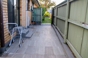A paved patio with a metal cart, a green fence, and a brick building. - Makers Rest a relaxing 4BR 3Bath for 6 with its own Poolfresh Wellness Retreat (Wynyard)