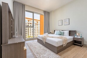 Ein Hotelzimmer mit einem großen Bett, einem Nachttisch mit Lampe, einer digitalen Uhr und Blick auf ein Gebäude durch das Fenster.