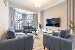 A modern living room with a sofa set, a coffee table, a TV, and a large window with curtains. - Stunning Gulf of Oman Views, 2BR with Assistant Room, Private Beach Access (Khor Fakkan)
