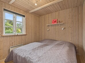 A bedroom with a large bed, wooden walls, a window, and a shelf with items. - "Erikgine" - 900m from the sea by Interhome (Væggerløse)