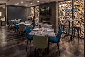 A restaurant with a modern interior, featuring tables with patterned tablecloths, blue chairs, and a large TV screen above a fireplace. - Steps from South Hills Village Mall + Restaurant (Pittsburgh)