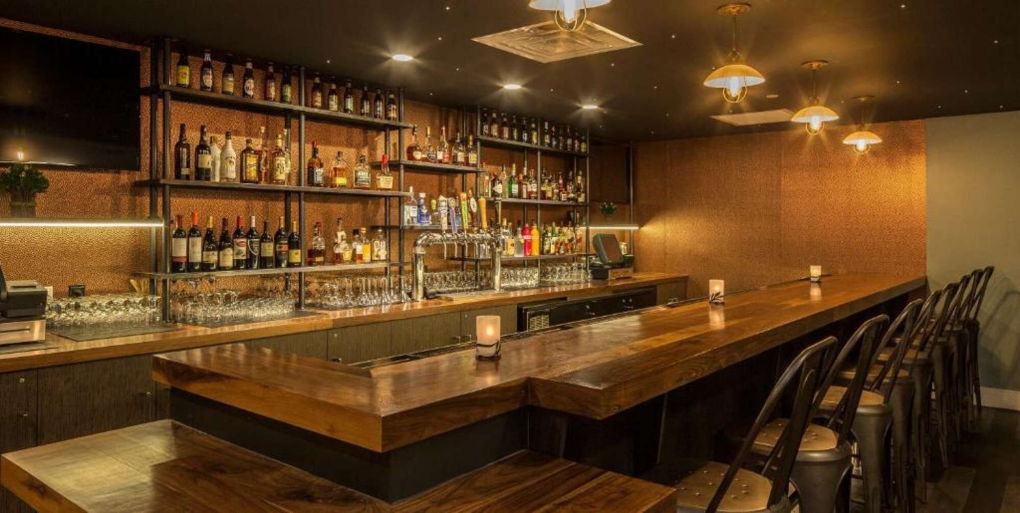 A bar area with wooden bar counters, shelves of liquor bottles, and bar stools.