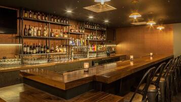 A bar area with wooden bar counters, shelves of liquor bottles, and bar stools.