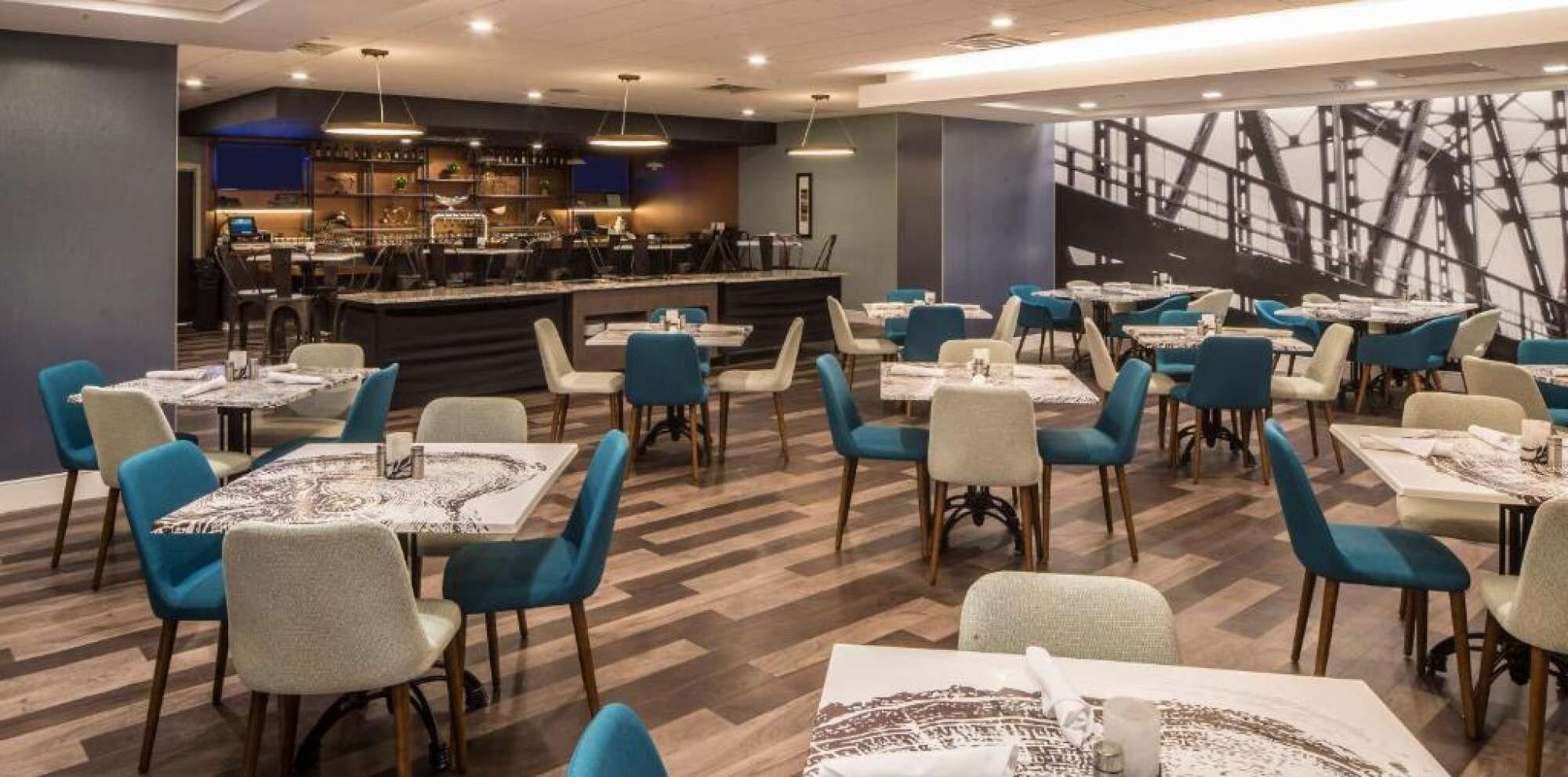 Un restaurante con varias mesas y sillas, una zona de bar y una pared decorada.