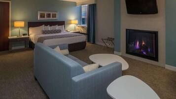 A hotel room with a bed, a sofa, a small table, a TV, and a fireplace.