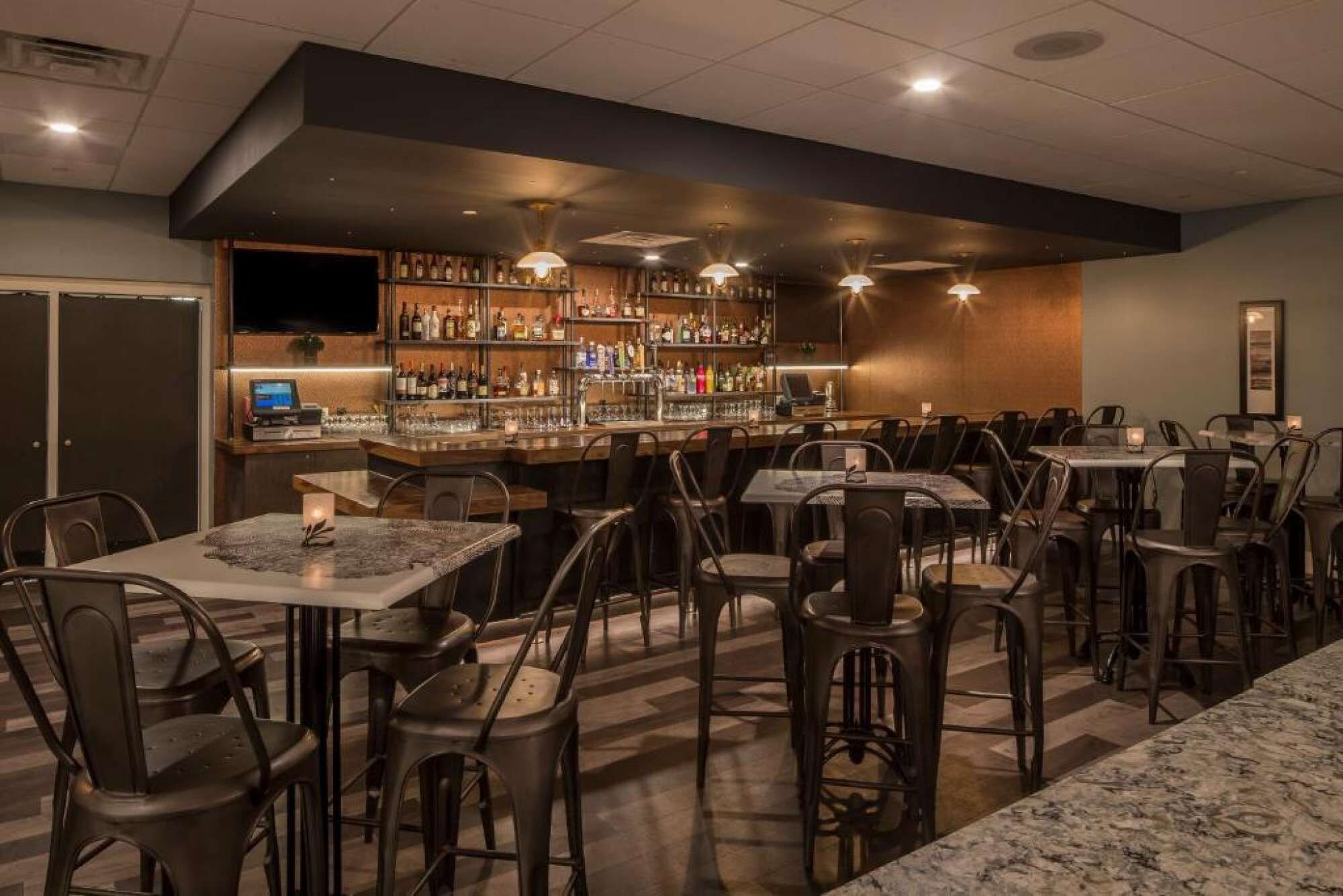 Zona de bar con diversas opciones de asientos, barra con una variedad de botellas y una pantalla de televisión.