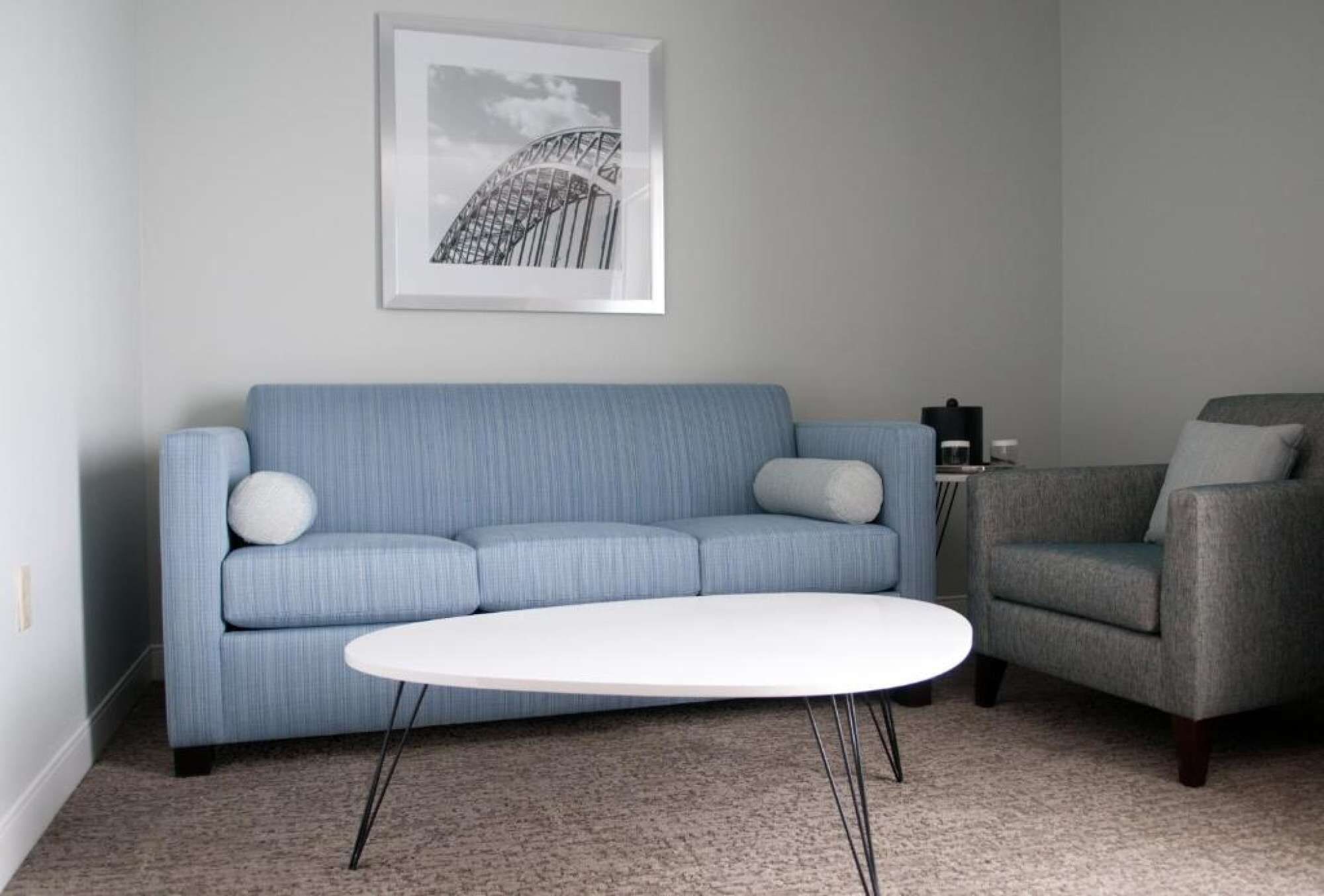 Una sala de estar con un sofá azul, una mesa de centro blanca y un sillón gris.