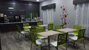 Un comedor con sillas y mesas verdes, una zona de cocina con electrodomésticos y una pared decorada con un adhesivo floral.