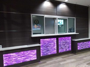 A reception area with a check-in/out sign, a television screen, and a purple-lit reception desk. - Downtown Stay + Free Breakfast & Parking (Houston)