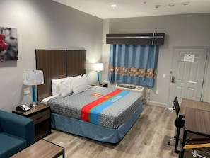 Habitación de hotel con cama, mesita de noche, lámpara y escritorio con silla.