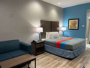 A hotel room with a bed, a blue sofa, a nightstand, and a table. - Downtown Houston + Free Breakfast & Parking (Houston)