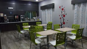 Un comedor con sillas y mesas verdes, una zona de cocina con electrodomésticos y una pared decorada con un adhesivo floral.