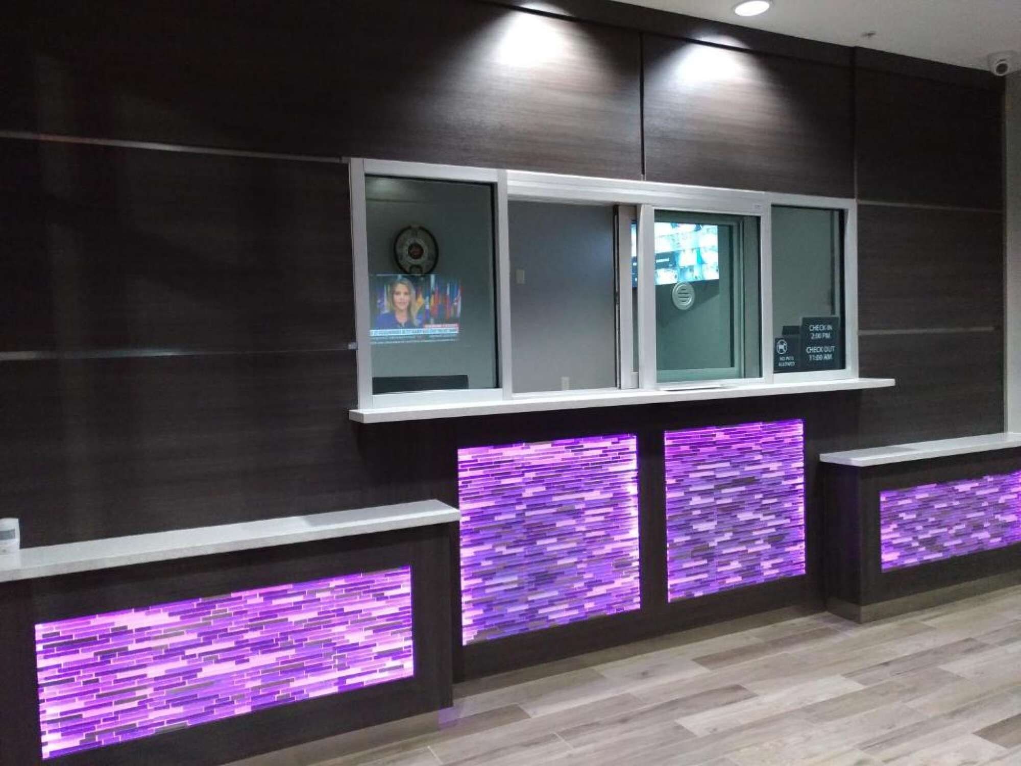 Un espace d’accueil avec un panneau indiquant les modalités d’enregistrement et de départ, un écran de télévision et un comptoir d’accueil éclairé de lumière violette.