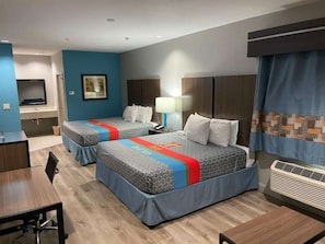 Habitación de hotel con dos camas, un escritorio, una silla, baño y ventana con cortinas.