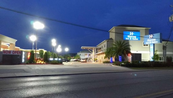 Un hotel con un letrero llamativo, un estacionamiento y una calle de noche.