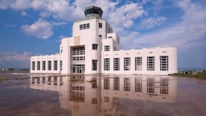 Un edificio grande y blanco con una torre central y numerosas ventanas, rodeado de una superficie húmeda y reflectante.
